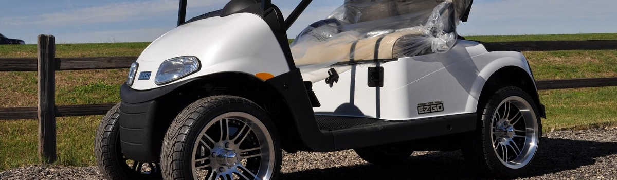 A close-up view of a white E-Z-GO® golf car with the seats still wrapped next to a wooden ranch fence.