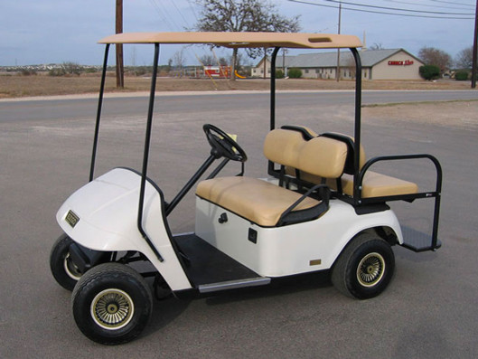 A four seater white golf cart by the street.